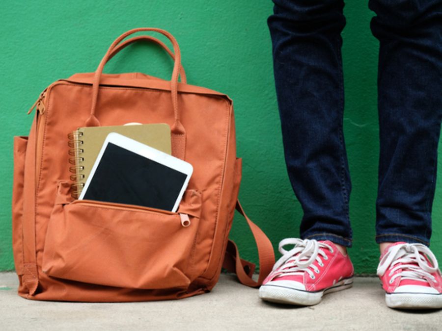 Nahhaufnahme auf Beine in Sneakers neben einem Schulrucksack